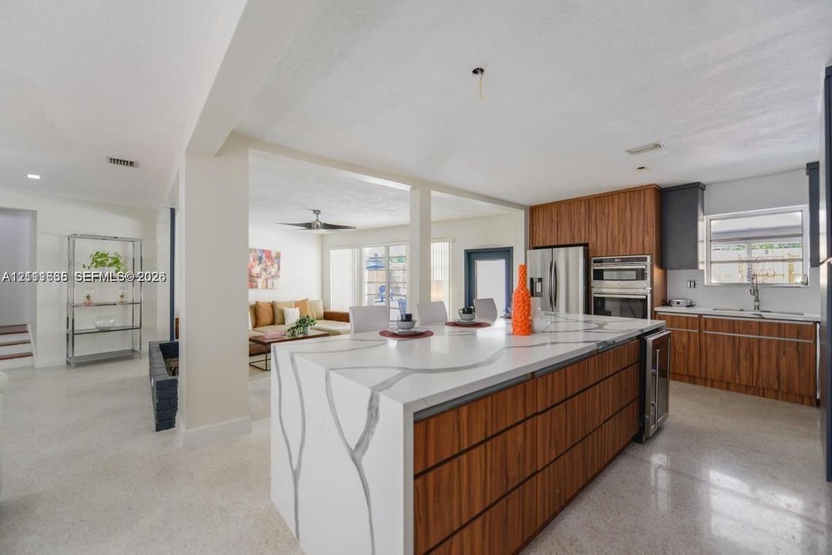 Kitchen featuring a central island with a stone-finish countertop and waterfall edge, wood-finish cabinetry, stainless steel built-in wall oven, and l