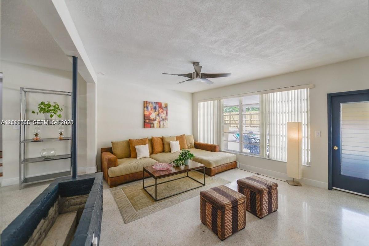 Living area featuring terrazzo flooring, a fireplace with a painted stone hearth, a central ceiling fan, and a glass-panel entry door