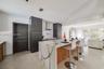 Kitchen featuring a waterfall-edge island with stone-finish countertops and wood-finish cabinetry, floor-to-ceiling dark charcoal pantry units, and a 
