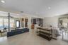 Open-concept interior featuring light-toned stone flooring, a painted brick structural partition, recessed lighting, and a kitchen equipped with dark 