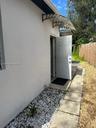 Exterior side entrance featuring a white panel door, decorative metal-frame awning, concrete paver path, and stone ground cover