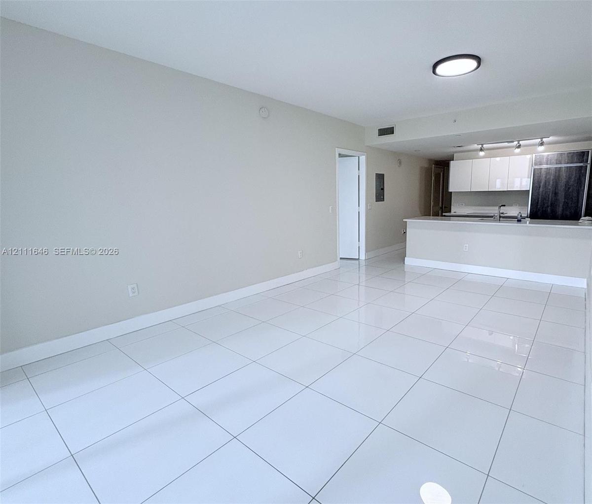Large-format white tile flooring, high-gloss white cabinetry, integrated stainless steel kitchen appliances, peninsula countertop, and flush-mount lig