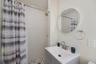 Bathroom featuring a gray vanity with an integrated basin, circular wall mirror, wall-mounted towel ring, and a tiled shower stall with a rain-style s