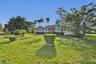Single-story residence featuring a tile roof, brick exterior accents, multi-pane windows, and a paved walkway situated on a lot with mature palm trees