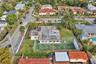 Aerial perspective of a corner lot property featuring a single-story residence, a private fenced-in sport court, expansive green space, and mature lan