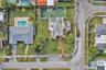 Aerial view of the property featuring a private fenced-in tennis court, expansive lawn, and paved walkway