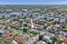 Corner-lot property featuring a multi-pitched roof, paved driveway, mature perimeter landscaping, and a central lawn area