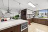 Kitchen featuring dual-toned cabinetry with high-gloss upper units and wood-finish lower units, light-toned stone-surface countertops, industrial-styl