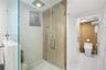 Walk-in shower with terrazzo-style wall and floor tiles, wood-slat accent wall, frameless glass enclosure, rain showerhead, and sliding door entry