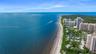 Coastal property featuring direct ocean frontage, expansive sandy beach, and proximity to mid-rise residential structures surrounded by mature tropica