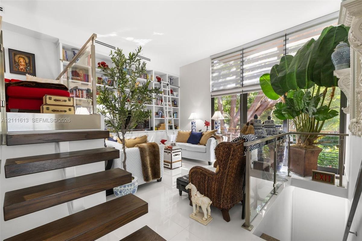 Floor-to-ceiling built-in library shelving with rolling ladder, high-gloss tile flooring, dark wood-finish open staircase, floor-to-ceiling windows wi