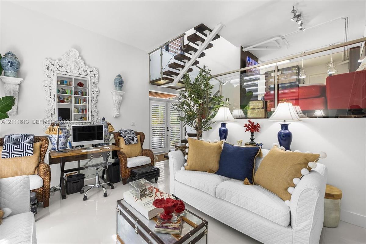 Open-concept interior featuring high ceilings, a floating staircase with glass railings, polished tile flooring, and integrated display shelving