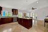 Kitchen featuring dark-toned cabinetry, a central island with built-in wine storage, stone countertops, large-format tile flooring, and a vaulted ceil