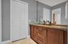Bathroom vanity featuring a stone countertop, dual glass vessel sinks, high-arc faucets, wood-finish cabinetry with metallic hardware, and a large wal