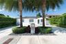 Single-story residence featuring a paved driveway with turf accents, mature palm trees, groomed privacy hedges, and a contemporary concrete mailbox pi