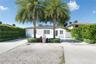 Single-story exterior featuring white stucco siding, a hip roof, expansive concrete paved driveway with integrated stone borders, mature palm trees, a