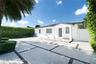 Exterior facade featuring a covered entryway, smooth white stucco finish, geometric concrete paver driveway with decorative stone accents, and manicur