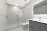 Walk-in glass-enclosed shower featuring stone-finish wall tile, rainfall showerhead, and built-in recessed shelving, complemented by a modern floating