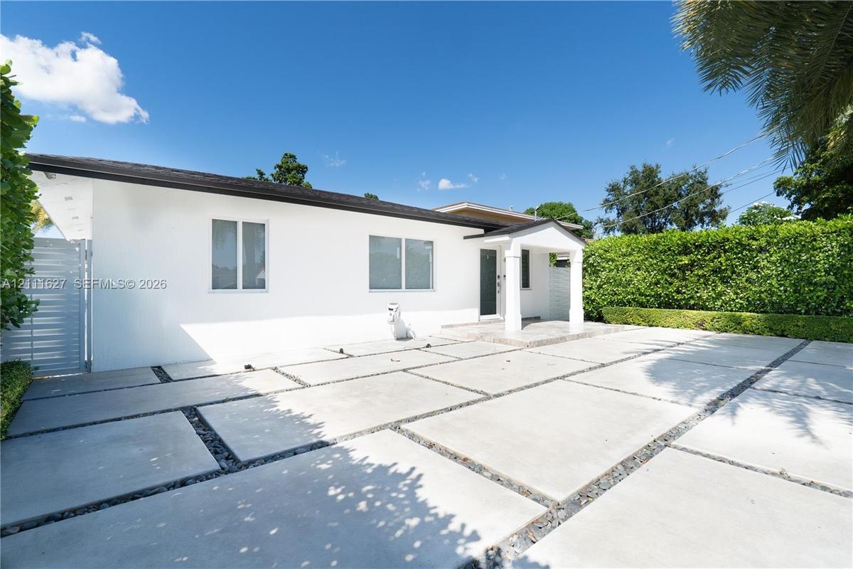 Single-story exterior featuring white stucco finish, large-format concrete paver driveway with decorative stone borders, covered entryway with support