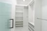 Custom walk-in closet featuring white built-in shelving, floor-to-ceiling storage units, multiple metal hanging rods, and stone-finish tile flooring