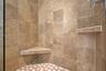 Walk-in shower featuring large-format neutral-toned tile walls, a built-in corner bench, a floating corner shelf, and a mosaic-tiled floor with metal 