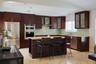 Kitchen featuring dark wood cabinetry, stainless steel appliances, a center island with built-in wine storage, stone countertops, and a glass tile bac