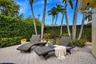 Paver patio featuring integrated pool edge, perimeter privacy hedges, and mature palm trees