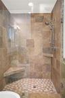 Walk-in shower featuring floor-to-ceiling stone-finish tile, a glass enclosure, dual shower
