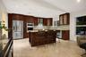 Kitchen featuring dark wood cabinetry, stainless steel appliances, built-in double wall ovens, a stone-surface center island, and tile flooring