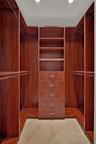 Custom walk-in closet featuring floor-to-ceiling wood-finish cabinetry, built-in shelving, a five-drawer dresser unit with metallic pulls, multiple in