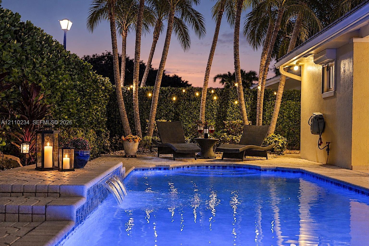 In-ground swimming pool featuring a tiered stone paver deck, integrated water feature, and mature palm trees