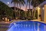 In-ground swimming pool featuring a tiered stone paver deck, integrated water feature, and mature palm trees