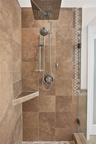 Walk-in shower featuring large-format earth-tone tile, a square rainfall showerhead with a secondary handheld sprayer, a built-in triangular corner sh