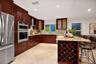 Kitchen featuring dark wood cabinetry, stainless steel double wall ovens, stone countertops, integrated wine storage, and neutral-tone tile flooring