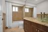 Bathroom featuring a wood-finish vanity with a stone countertop, glass vessel sink, mosaic tile tub surround, and large wall-mounted mirror