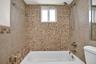 Bathroom featuring a porcelain soaking tub with metallic faucet fixtures, multi-textured square mosaic wall tiles, and a double-hung window