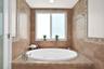 Oversized jetted soaking tub featuring a tile-surround deck, mosaic tile accents, polished chrome fixtures, and a dual-pane window