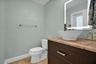 Dark wood vanity featuring a stone countertop, white vessel sink, brushed metal faucet, and an integrated LED-backlit mirror