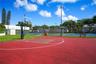 Outdoor recreation area featuring a paved basketball court, fenced tennis court, perimeter lighting, and surrounding green space