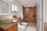 Bathroom featuring a frosted glass vessel sink, stone vanity countertop, lighted vanity mirror, and a walk-in shower with tiled walls, built-in bench,
