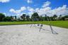Outdoor recreation area featuring a sand-surfaced ground, metal swing set, and an expansive grass lawn