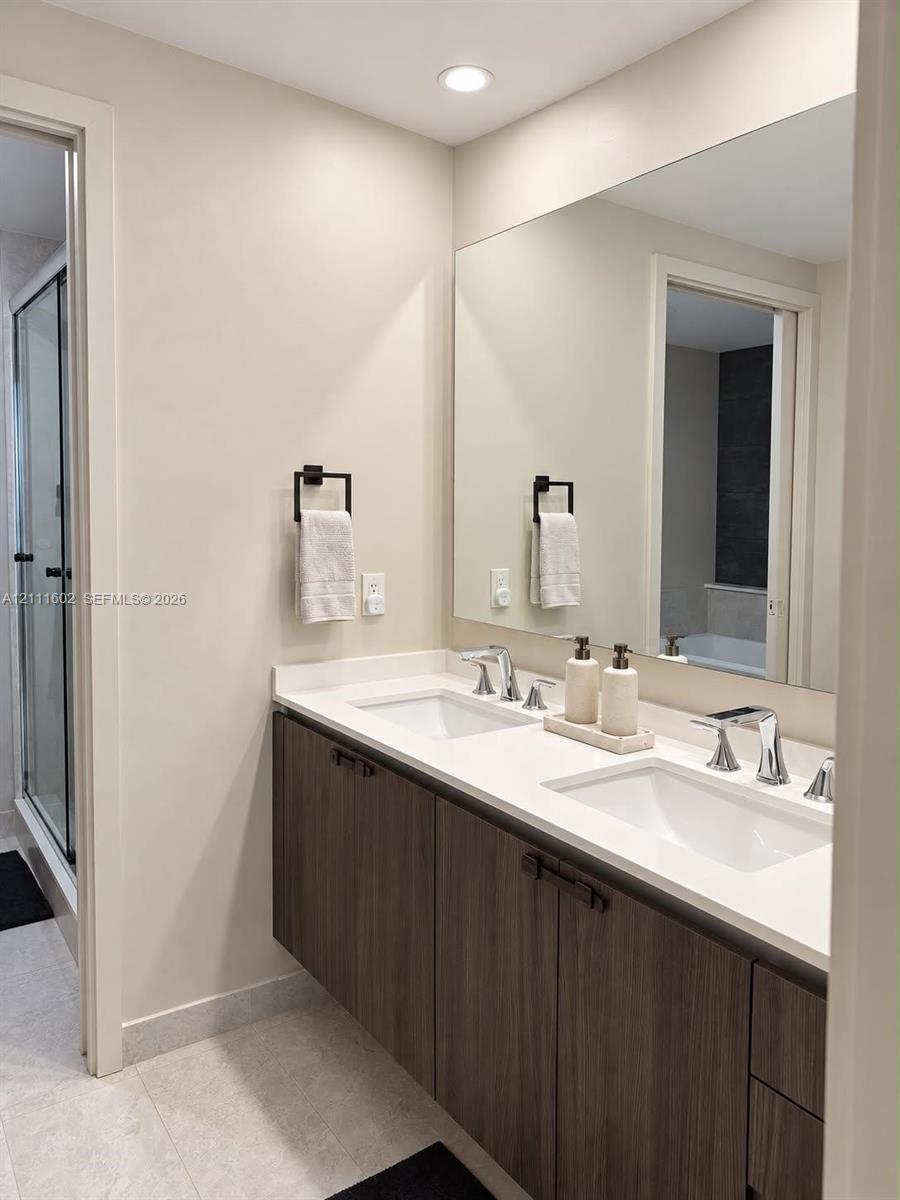 Floating wood-finish vanity with a double-sink white countertop, large wall-mounted mirror, matte black hardware, and recessed lighting
