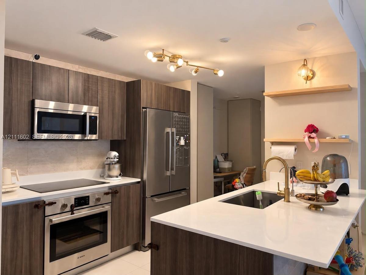 Kitchen featuring flat-panel wood-finish cabinetry, quartz countertops, stainless steel appliances, a multi-light brass fixture, and floating wooden s