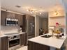 Kitchen featuring flat-panel wood-finish cabinetry, quartz countertops, stainless steel appliances, a multi-light brass fixture, and floating wooden s