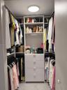 Walk-in closet featuring white built-in shelving, four integrated storage drawers with silver-tone pulls, multiple hanging rods, and a flush-mount ove