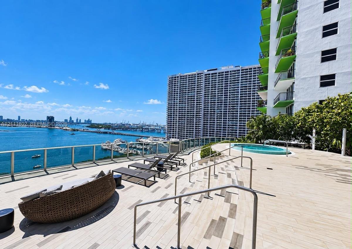 Expansive terrace featuring light-toned tile flooring, built-in circular spa, tiered levels with metal handrails, and glass perimeter railings