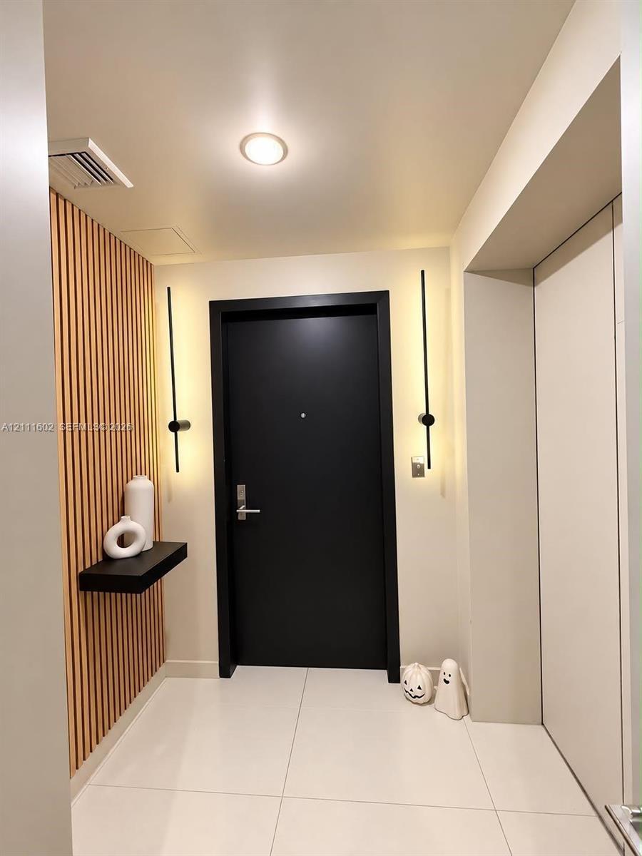 Entryway featuring vertical wood slat paneling, large-format tile flooring, a matte black door, dual linear wall-mounted light fixtures, and a floatin