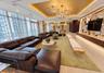 Expansive room featuring floor-to-ceiling windows, gold-leaf tray ceiling, branching metallic statement chandelier, light-toned wood-finish flooring, 