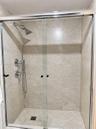 Walk-in shower featuring floor-to-ceiling stone-finish tile surround, sliding glass enclosure, polished chrome shower head, handheld sprayer, and diag