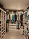 Walk-in closet featuring extensive built-in white shelving, multiple hanging rods, four deep storage drawers, and integrated overhead lighting